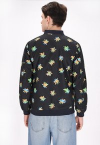 Zwarte bomberjack met een kleurrijke palmboomprint, geribde kraag en manchetten, met een zachte, glanzende textuur. Losse pasvorm.