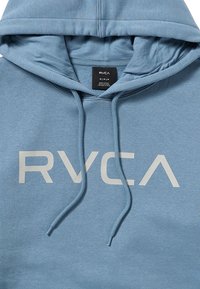 Haut à capuche bleu clair en tissu doux, comportant un grand logo "RVCA" blanc à l'avant et des cordons de serrage réglables au niveau de la capuche.