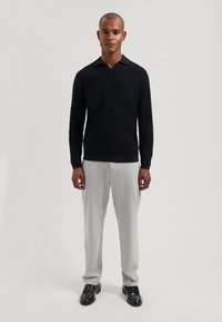 Czarny sweter dziany o fakturowanej powierzchni z kołnierzykiem, zestawiony z jasnoszarymi spodniami i czarnymi butami. Prosty, dopasowany fason.