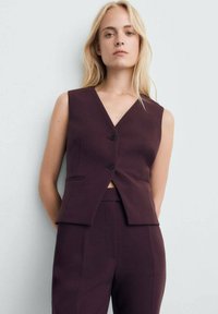 Bordeaux mouwloze vest met een V-hals, twee frontzakken en een cropped ontwerp, met twee knopen aan de voorkant. Draagt met bijpassende broek.