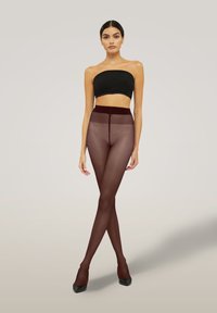 Calze sheer marroni con un alto pantalone, abbinate a un top nero senza spalline. Tessuto con texture e finitura liscia, indossato con tacchi neri.