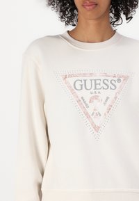 Crèmekleurige sweatshirt met een driehoekige grafiek, een glinsterende roze rand, zilveren tekst en studs. Van katoenmix materiaal.