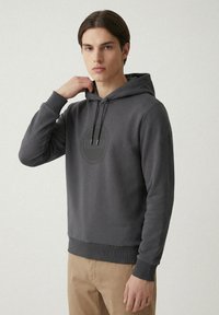 Grå hoodie tillverkad av mjukt tyg, med en pungficka, justerbar huva med dragsko och ribbade ärmslut och nederkant. Diskret logodetalj.