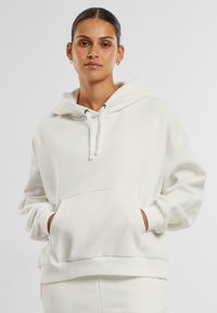 Kremhjorte med oversized passform, snorhette, kengurulomme, ribbestrikkede ermer og kant. Mykt stoff med minimalistiske designelementer.