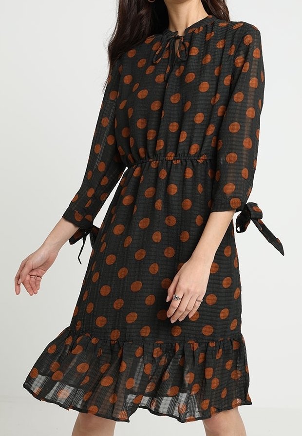 Černé šaty s hnědými puntíky, dlouhé rukávy se stahovacími detaily, zúžený pas a volánkový lem. Lehká, texturovaná tkanina.