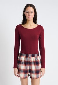 Body de manga larga burdeos combinado con pantalones cortos de cuadros en colores rojo, marino y crema, con cintura elástica y detalles de botones.