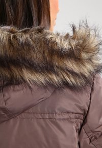 Brun isolerad jacka med en huva av konstpäls i mörk och ljusbrun textur. Slät tyg med synliga sömdetaljer.