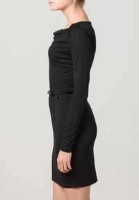 Robe noire ajustée avec manches longues, encolure arrondie et taille ceinturée. Confectionnée dans un tissu lisse et extensible, mettant en valeur la silhouette.