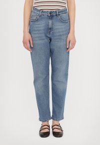 Jeans de denim azul claro con pierna recta, bolsillos frontales y una cinturilla clásica. Llevados con zapatos negros de estilo con tiras.