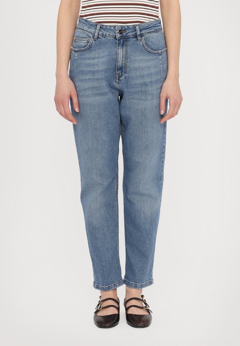 Jeans de denim azul claro con pierna recta, bolsillos frontales y una cinturilla clásica. Llevados con zapatos negros de estilo con tiras.