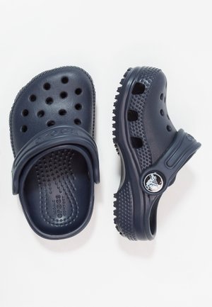 Sabots Crocs bleu marine avec trous de ventilation, semelles texturées et brides ajustables au talon sur fond blanc.