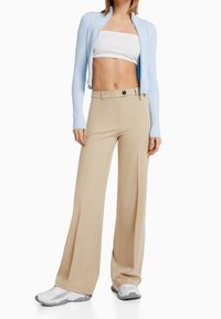 Vaaleansininen urheilullinen neuletakki, valkoinen cropped-paita ja beigekarvaiset leveälahkeiset housut napituksella. Harmaat lenkkarit viimeistelevät asukokonaisuuden.