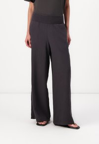 Pantaloni a gamba larga realizzati in tessuto testurizzato di un grigio scuro con vita arricciata, caratterizzati da una vestibilità ampia e una silhouette fluida.