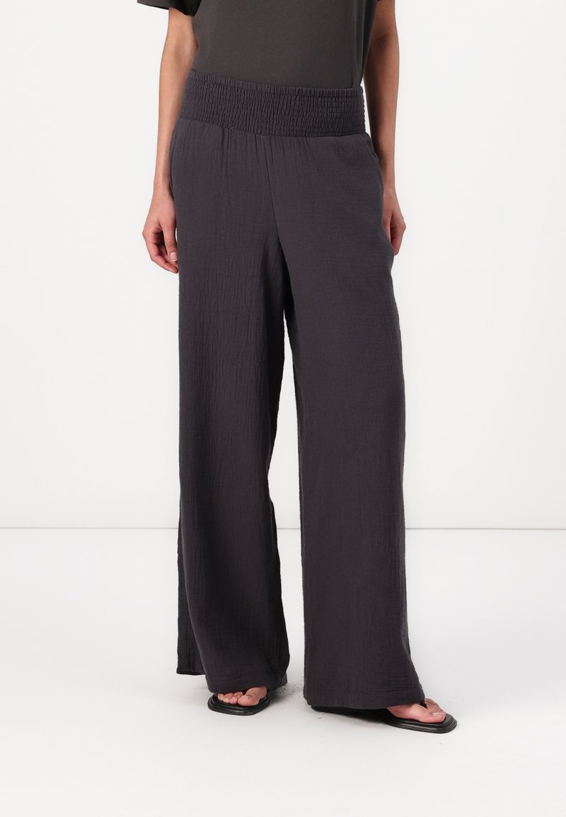 Wide-leg pants made of textured, dark gray fabric with a smocked waistband, featuring a loose fit and flowy silhouette.