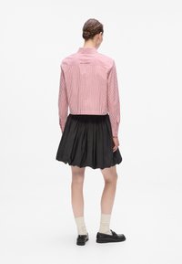 Rot-weiß gestreifte Button-Down-Bluse mit langen Ärmeln, kombiniert mit einem schwarzen Faltenrock. Der Stoff wirkt glatt mit einer strukturierten Passform.