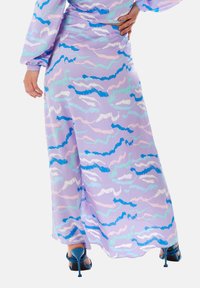 Purple maxi dress with wavy patterns in blue, light blue, and pink. Long sleeves, relaxed fit, paired with blue heeled sandals.