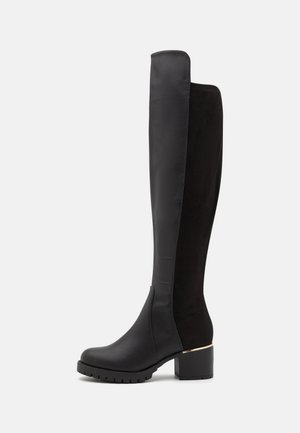 Botte haute noire pour femme combinant l'avant en cuir lisse avec l'arrière en suède, talon bas épais et semelle crantée.