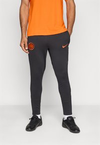 Melnas sporta bikses ar oranžu logotipu un akcentiem. Pieguļošs dizains, gluda tekstūra un elastīga josta. Saskaņotas ar melniem apaviem un baltām zeķēm.