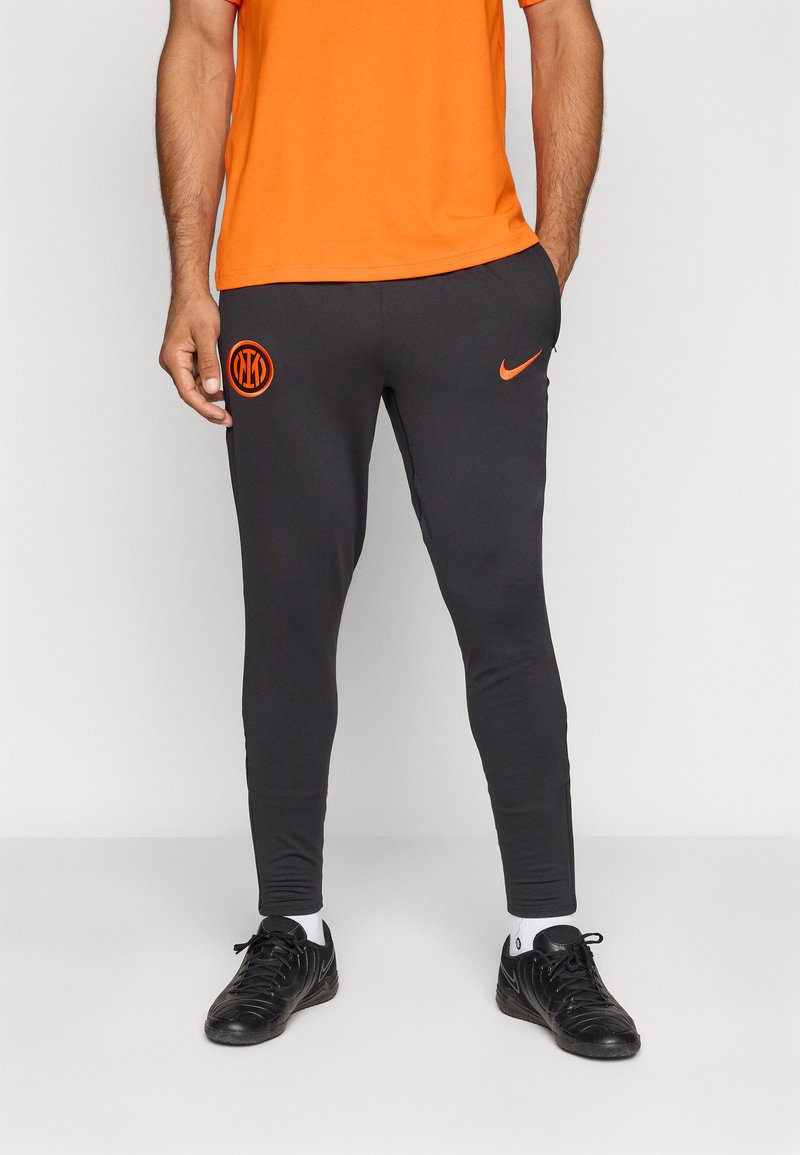 Melnas sporta bikses ar oranžu logotipu un akcentiem. Pieguļošs dizains, gluda tekstūra un elastīga josta. Saskaņotas ar melniem apaviem un baltām zeķēm.