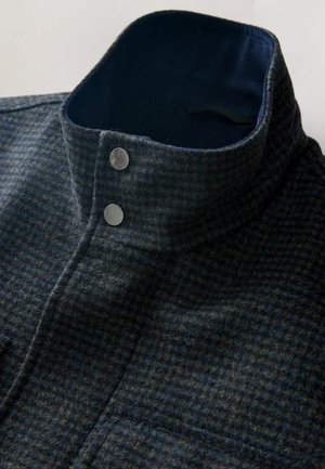 Dunkelblauer Musterkragen aus strukturiertem Stoff mit zwei silbernen Knöpfen und einem kontrastierenden marineblauen Innenfutter.