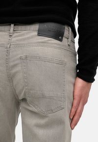 Gray denim jeans with a back pocket, textured fabric, and a black leather patch embossed with "INDICODE" near the waistband.