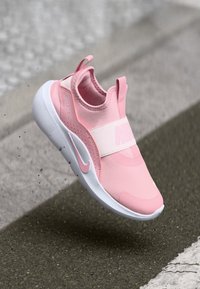Różowe sneakersy Nike na slip-on z gładką górą z tkaniny, elastycznym paskiem i białą podeszwą. Posiadają logo oraz teksturowane akcenty zapewniające przyczepność.