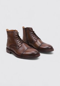 Botines de cuero marrón con un acabado suave, punta redondeada, cordones en la parte delantera, cremallera lateral y un tacón bajo y apilado.