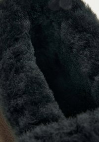Black fuzzy inner lining of a boot, featuring soft, plush texture. The exterior appears brown with a smooth, possibly leather finish.