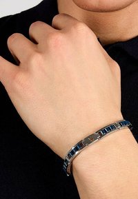 Metallarmband med blå inläggsbitar, en polerad silverfinish och en centralt rektangulär lås med en logotyp.