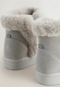 Graue Wildleder-Stiefeletten mit weichem Kunstfellfutter, flacher Gummisohle und kontrastierendem, weichem Textilbund. Markenlabel an der Seite sichtbar.