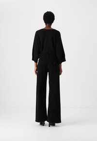 Μαύρος oversized πουλόβερ με φαρδιές μανσέτες, συνδυασμένο με ψηλόμεσες μαύρες φαρδιές παντελόνες. Λιτές γραμμές, ομαλή υφή και χωρίς σχέδια.