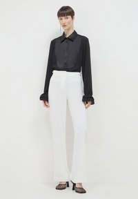 Chemise noire à manches longues avec un devant en satin, boutons, pantalon blanc taille haute et chaussures à talons en mesh noir. Texture lisse, coupe sur mesure.