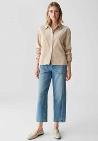 Camicia a righe beige con bottoni e maniche lunghe, abbinata a jeans larghi azzurri e scarpe beige senza lacci.