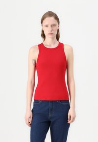 Rød ribbet tank-top med rund hals og uten ermer, som komplementerer mørkeblå denimjeans.