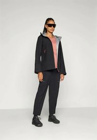 Čierna nepremokavá bunda so šedým vnútrom, vybavená kapucňou a zipsovými detailmi, v kombinácii s tmavými nohavicami a čiernym obuvou.