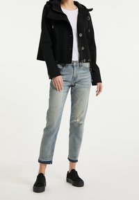 Schwarze, gekürzte Jacke mit Kapuze, ausgestattet mit großen Knöpfen, kombiniert mit hellblauen, verwaschenen Jeans und schwarzen Plateausneakern.