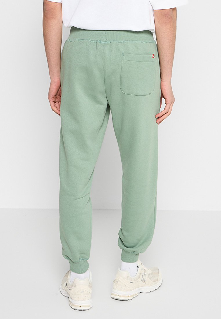 Mintgrüne Jogginghose aus weichem Material, mit schmal zulaufendem Bein, elastischem Bund, einer Gesäßtasche und gerippten Bündchen. Getragen mit weißen Sneakers.