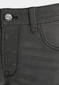 Jeans de denim cinza com um botão metálico com logótipo, detalhes cosidos e um tecido suavemente texturizado. A cintura é levemente elástica.
