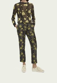 Top de manga larga floral en negro con patrones amarillos, combinado con pantalones florales negros. Zapatillas crema completan el conjunto.