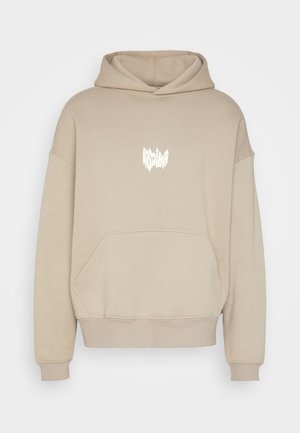 Beżowa bluza z kapturem z kieszenią z przodu oraz białym zniekształconym tekstowym logo na środku klatki piersiowej.