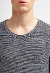 Suéter gris texturizado con un cuello redondo. La tela presenta un patrón de canalé y diferentes tonalidades de gris a lo largo.