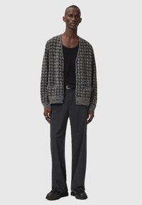 Strukturert grå cardigan med houndstooth-mønster, åpen front, kombinert med en svart tank topp og mørkegrå, løstsittende bukser. Svarte sko.