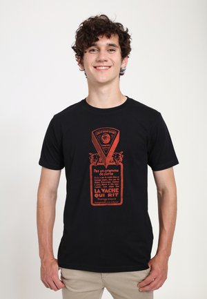 Black cotton t-shirt featuring a large red graphic illustration of a cheese product label with text in French, depicting cows and a globe design.