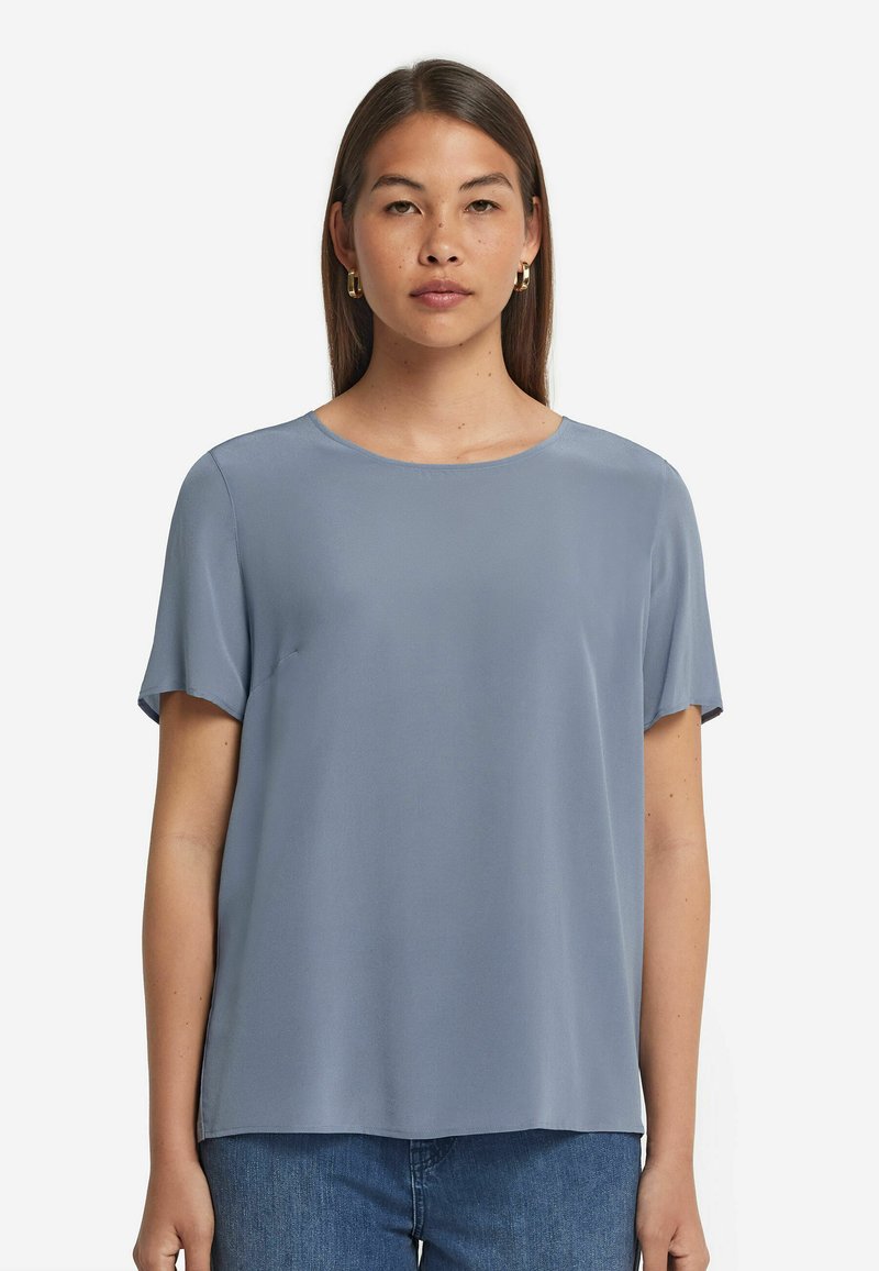 Ljust blå blus i mjukt tyg, med korta ärmar och rundad halsringning. Kombinerad med blå denimjeans.