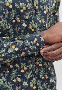 Mørkeblå skjorte med et botanisk mønster med gule appelsiner, grønne blade og hvide blomster; button-down-krave med manchet detaljer.