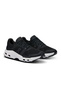 Scarpe sportive nere realizzate in mesh e materiali sintetici, con una suola bianca, forma curvilinea e fori di ventilazione sulla suola.