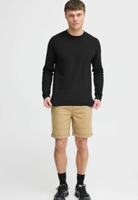 Zwarte long sleeve shirt, khaki shorts met opgerolde mouwen, gecombineerd met zwarte sokken en schoenen. Eenvoudig ontwerp en casual uitstraling.
