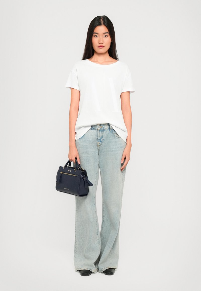T-shirt blanc à manches courtes avec un motif subtil, jean clair à jambes larges, et un petit sac à main bleu marine avec des accessoires en or.