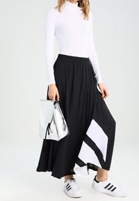 Svart maxikjol med vit randig accent, tillsammans med en tajt vit polo-tröja och en silverryggsäck. Bärs med vita sneakers.