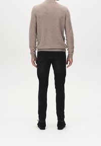 Krémový pletený svetr s vysokým límcem, kombinovaný s černými slim fit džíny a černými botami, viděný ze zadní strany.